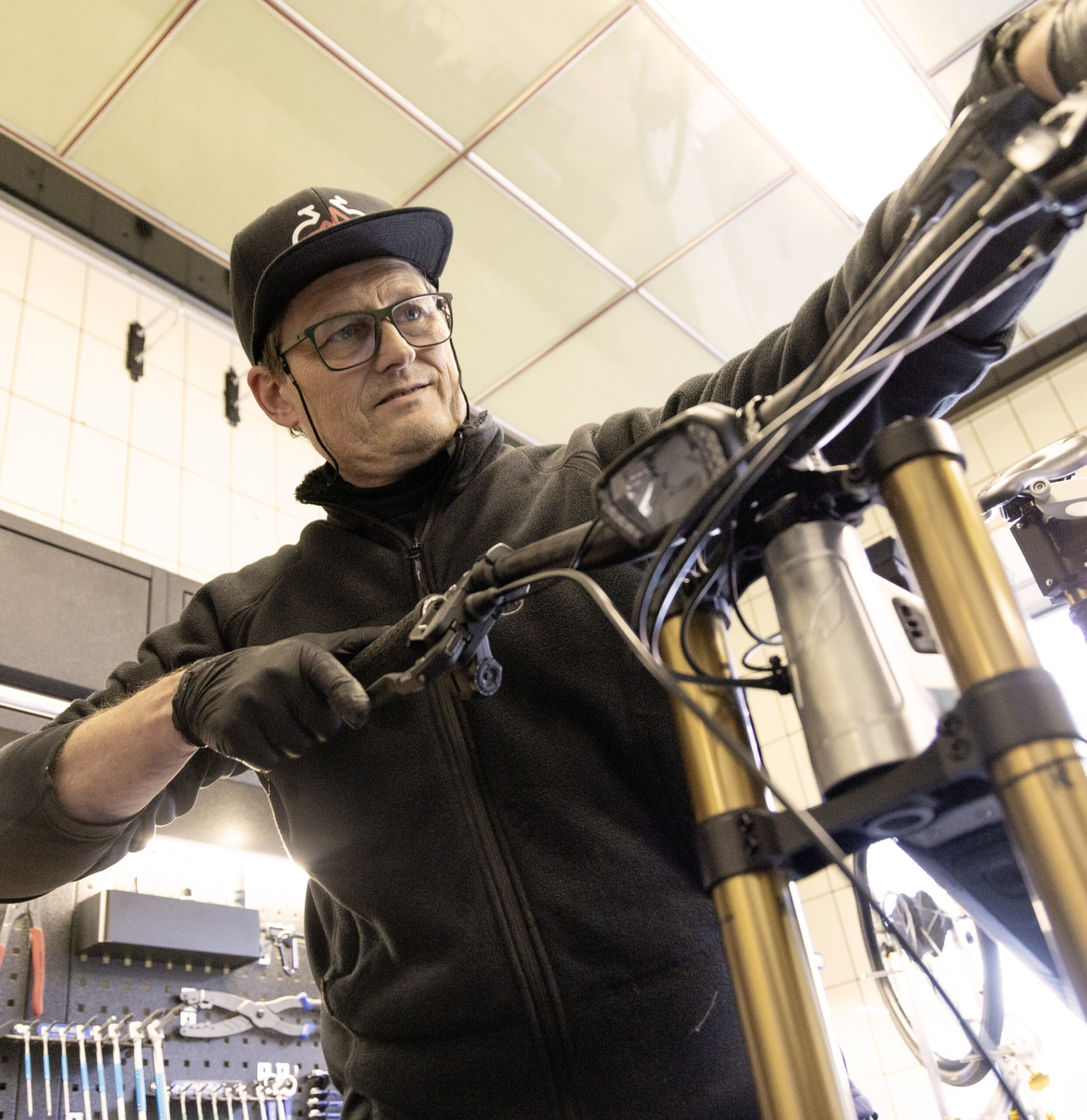 Mechaniker in einer Fahrradwerkstatt arbeitet konzentriert am Lenker und der Federgabel eines Mountainbikes.
